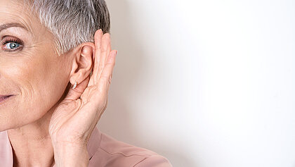 Eine ältere Dame hält ihre Hand hinterm Ohr