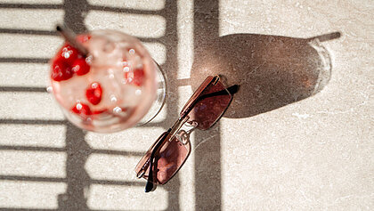 Nahaufnahme einer rosa Sonnenbrille mit Getränk