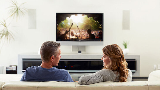Zwei Personen sitzen auf dem Sofa vor einem Fernseher