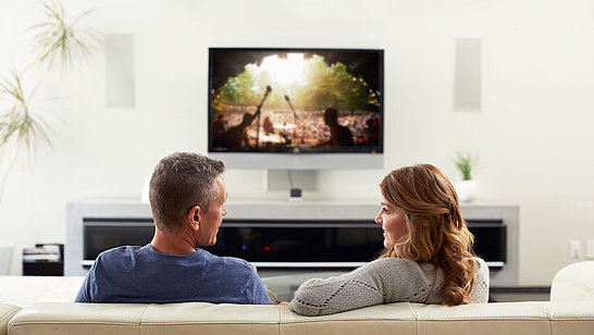 Zwei Menschen unterhalten sich, im Hintergrund ist ein Fernseher zu sehen