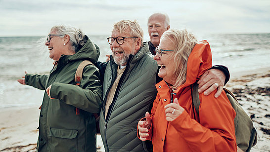 Eine Gruppe älterer Damen und Herren am Strand mit Windjacken