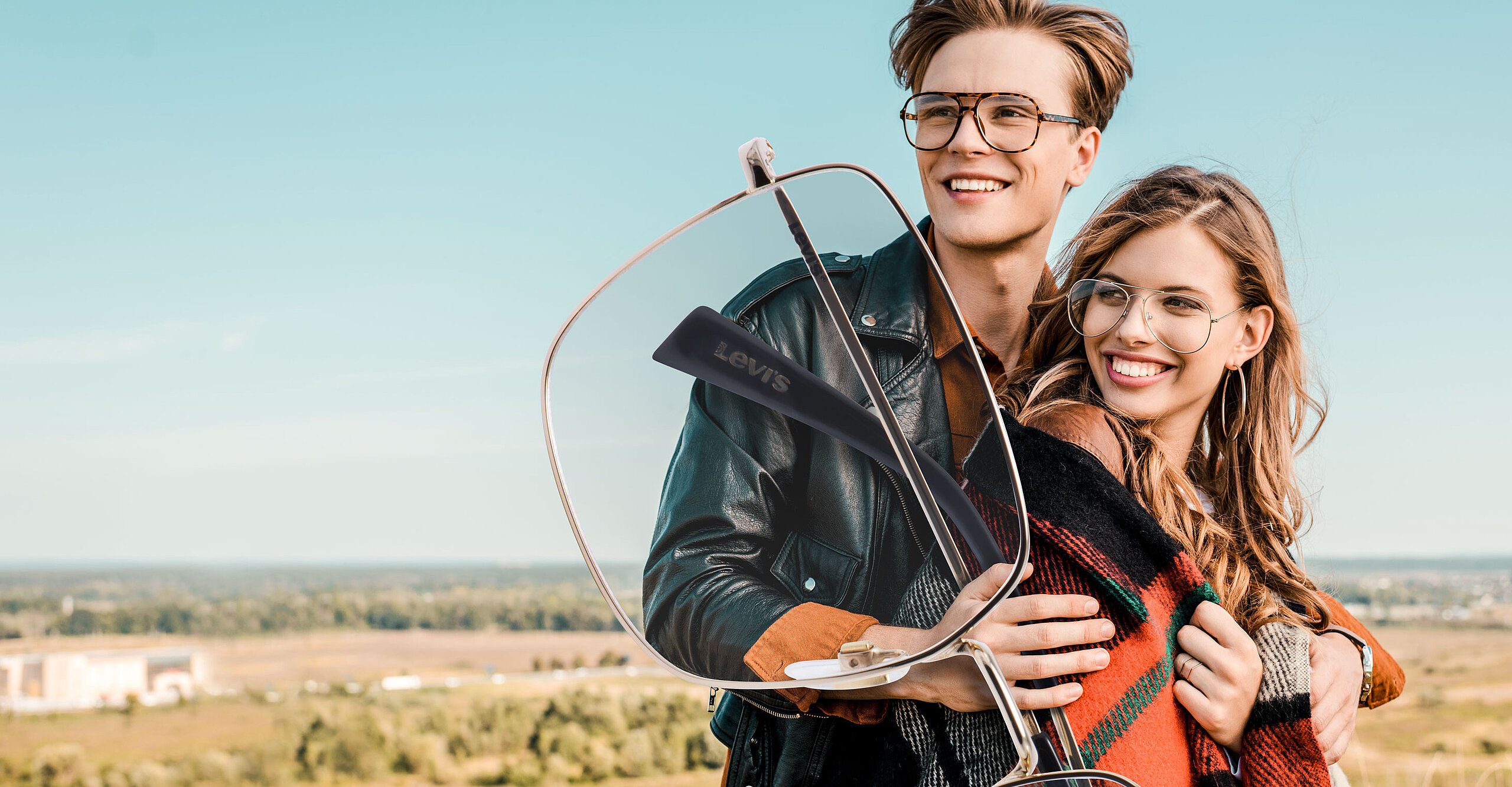 Junge Dame und Herr mit Brille im Freien halten eine große Brille in der Hand