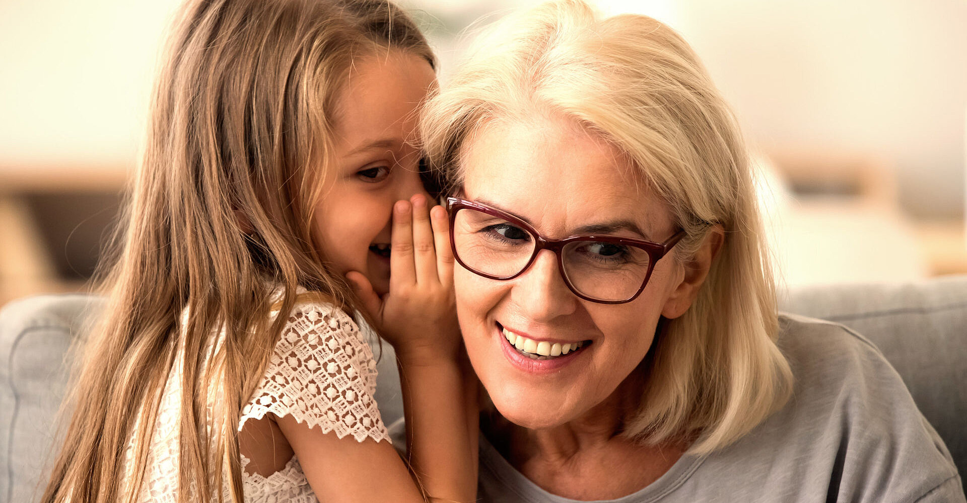 Ein Mädchen flüstert einer älteren Dame mit Brille etwas ins Ohr