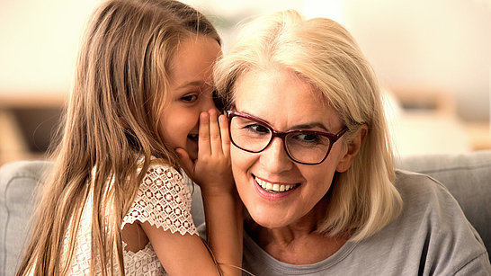 Ein Mädchen flüstert einer älteren Dame mit Brille etwas ins Ohr