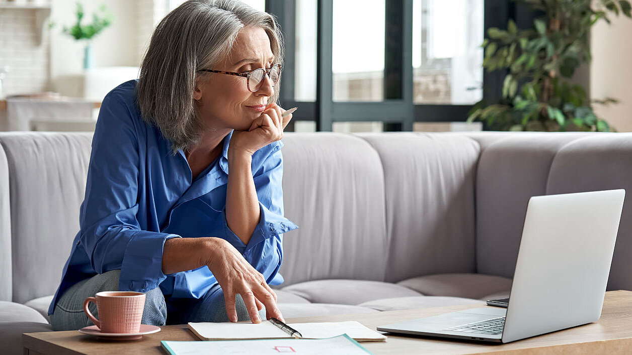 Ältere Dame mit Brille sitzt vor ihrem Laptop