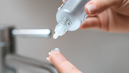 Pflegemittel wird auf eine Kontaktlinse getropft