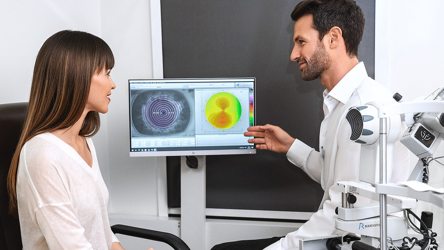 Ein Augenoptiker erklärt einer Dame Aufnahmen eines Sehtests 