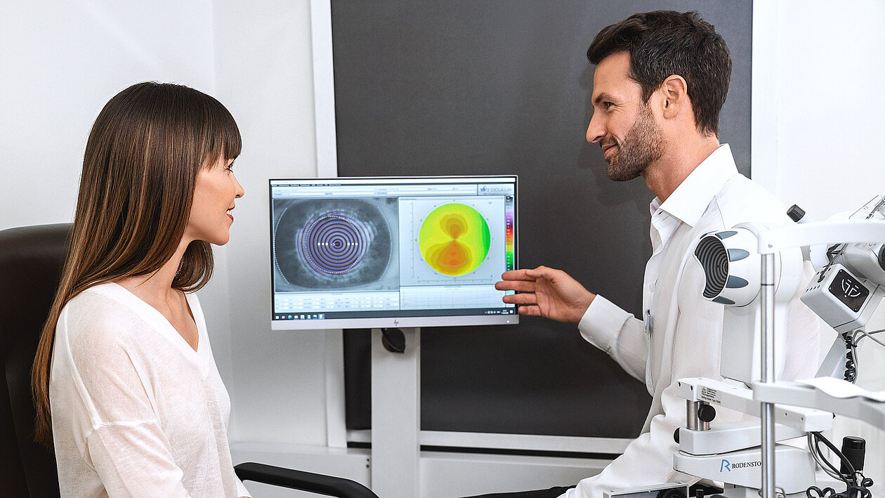Ein Augenoptiker erklärt einer Dame Aufnahmen eines Sehtests 