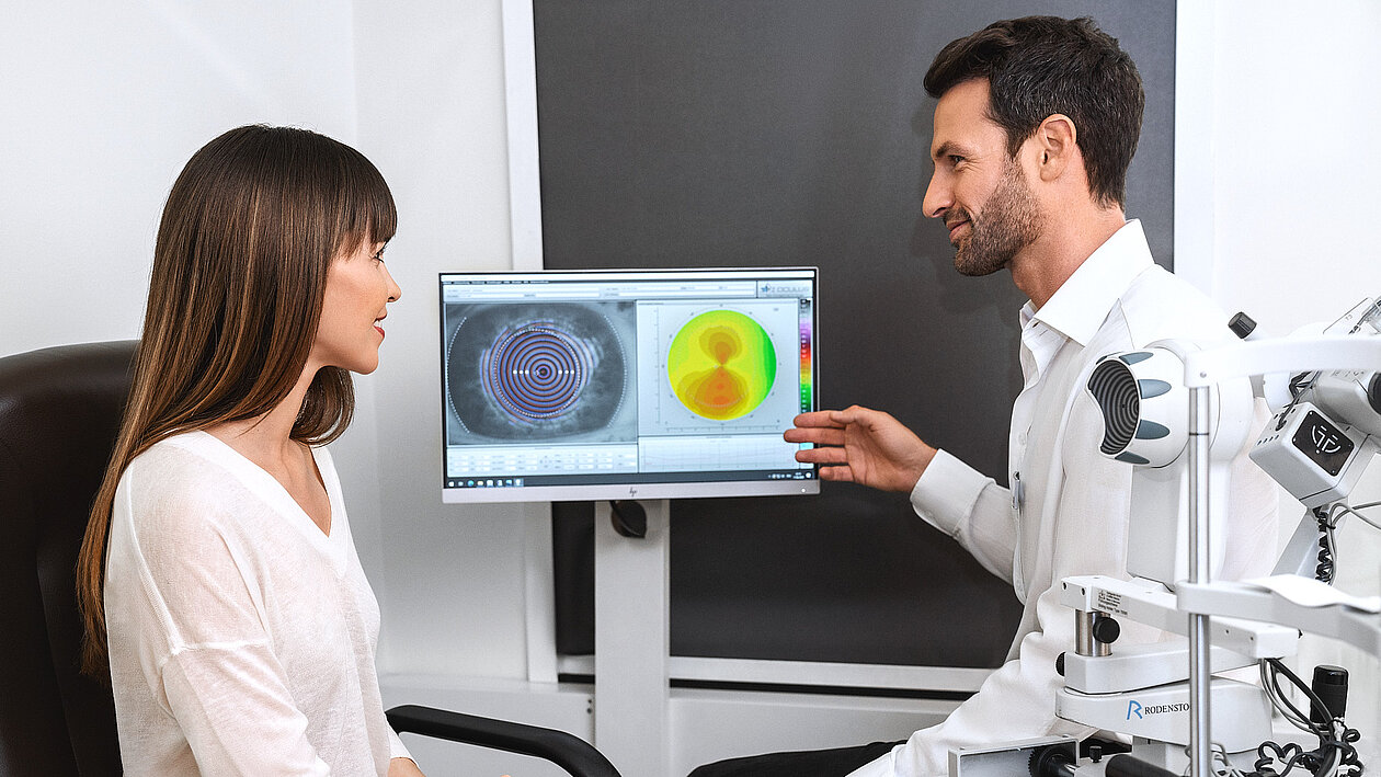 Ein Augenoptiker erklärt einer Dame Aufnahmen eines Sehtests 