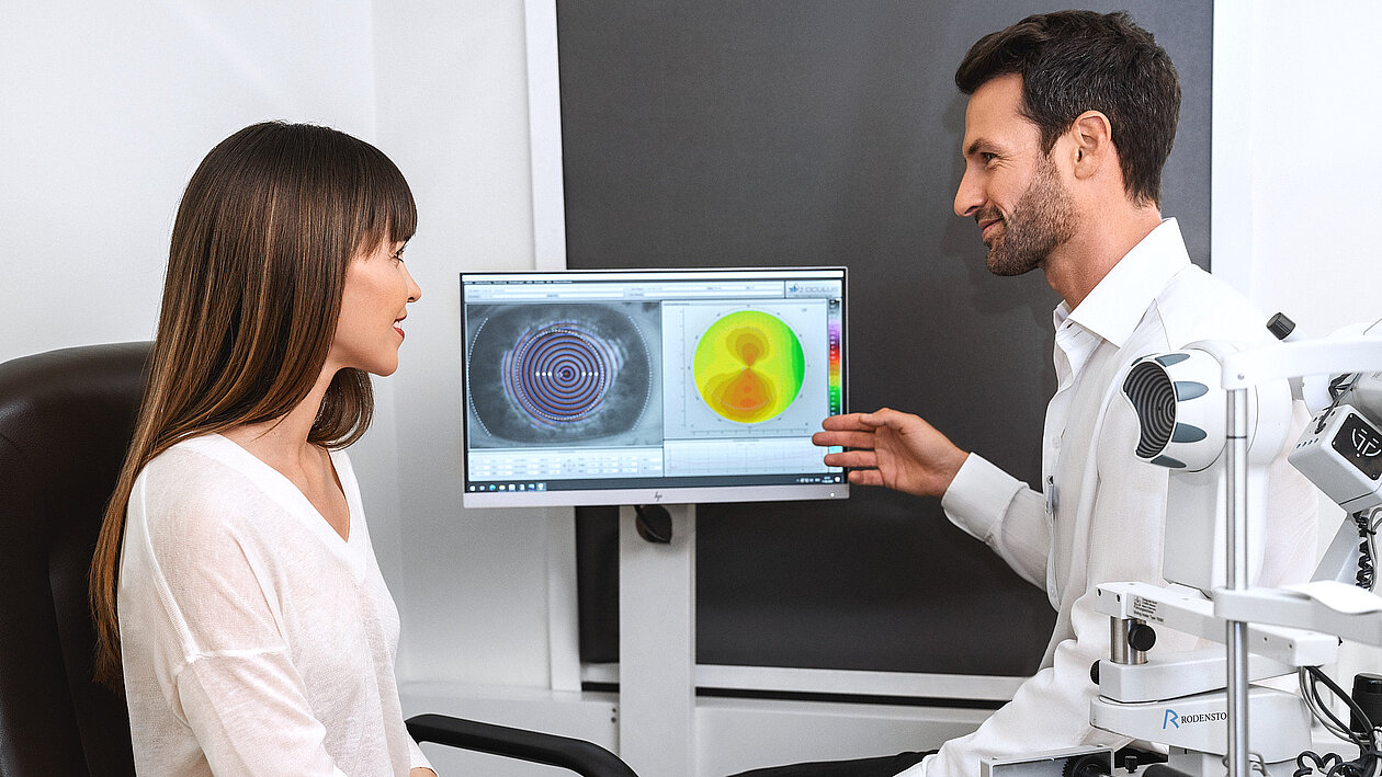 Ein Augenoptiker erklärt einer Dame Aufnahmen eines Sehtests 