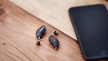 Zwei Hörgeräte liegen neben einem Smartphone